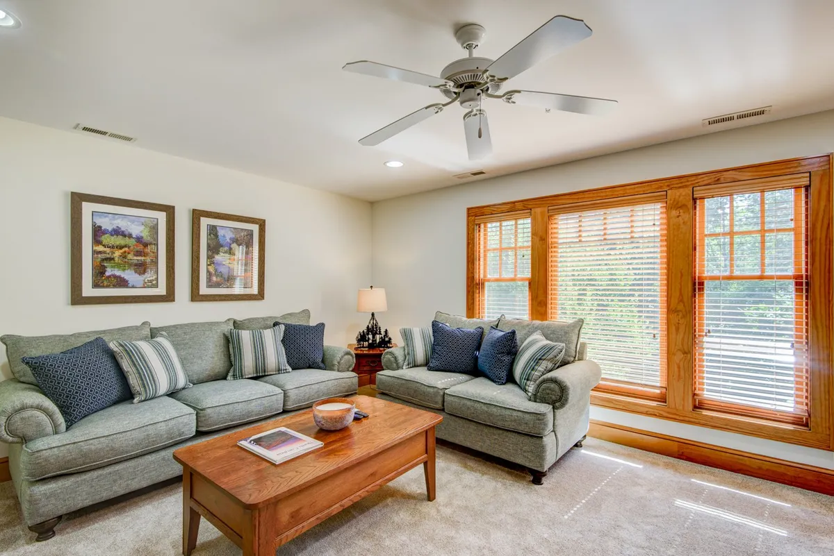 A cozy living room with a sofa adorned with decorative cushions, a coffee table, wall artwork, and large windows with wooden blinds. The inviting scene suggests moments of relaxation, socializing, and enjoying the mountain view from indoors.