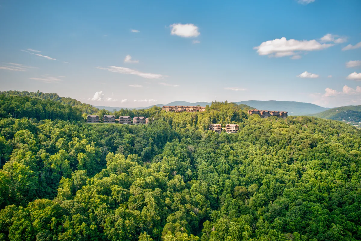 A wide, scenic landscape featuring rolling mountains, lush green trees, and a cluster of charming hillside buildings. The view feels expansive and serene, ideal for photography, relaxation, and appreciating nature's beauty.