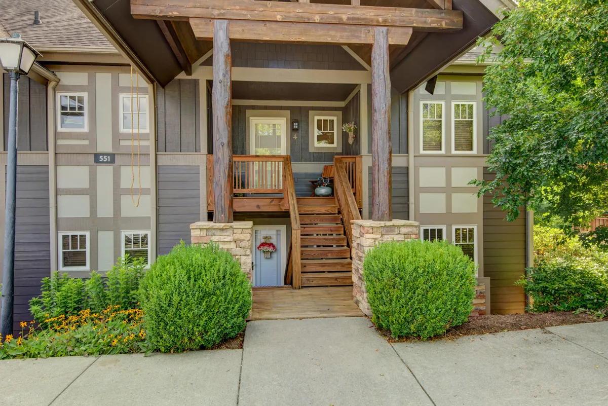 A charming wooden front porch with stone steps, surrounded by green shrubs and flower beds. The inviting porch overlooks a vibrant outdoor setting, hinting at a welcoming home base after a day of exploration.