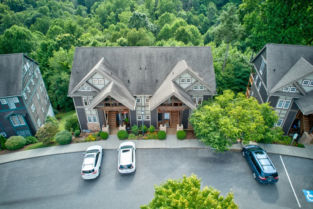 This image showcases a two-story building within the Echota community, surrounded by landscaped gardens and a parking area with vehicles. The multiple entrances and ample outdoor space suggest a vibrant, communal environment where neighbors can gather and interact.