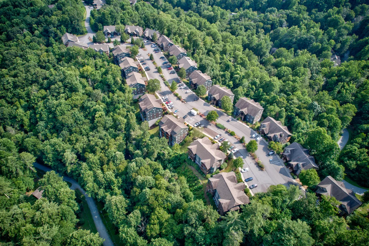 A peaceful, well-maintained Echota community landscape with clusters of residential buildings nestled among lush greenery and winding pathways. Residents are seen strolling or biking along the paths, while open spaces invite community gatherings or family picnics. The natural setting highlights the opportunities for outdoor recreation and the harmonious integration of the built environment with its scenic surroundings.