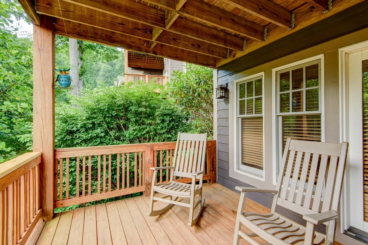A tranquil wooden deck furnished with classic rocking chairs, protected by a wooden railing, and encircled by lush greenery. The porch invites relaxation and offers a quiet spot for enjoying sunrise or sunset views.