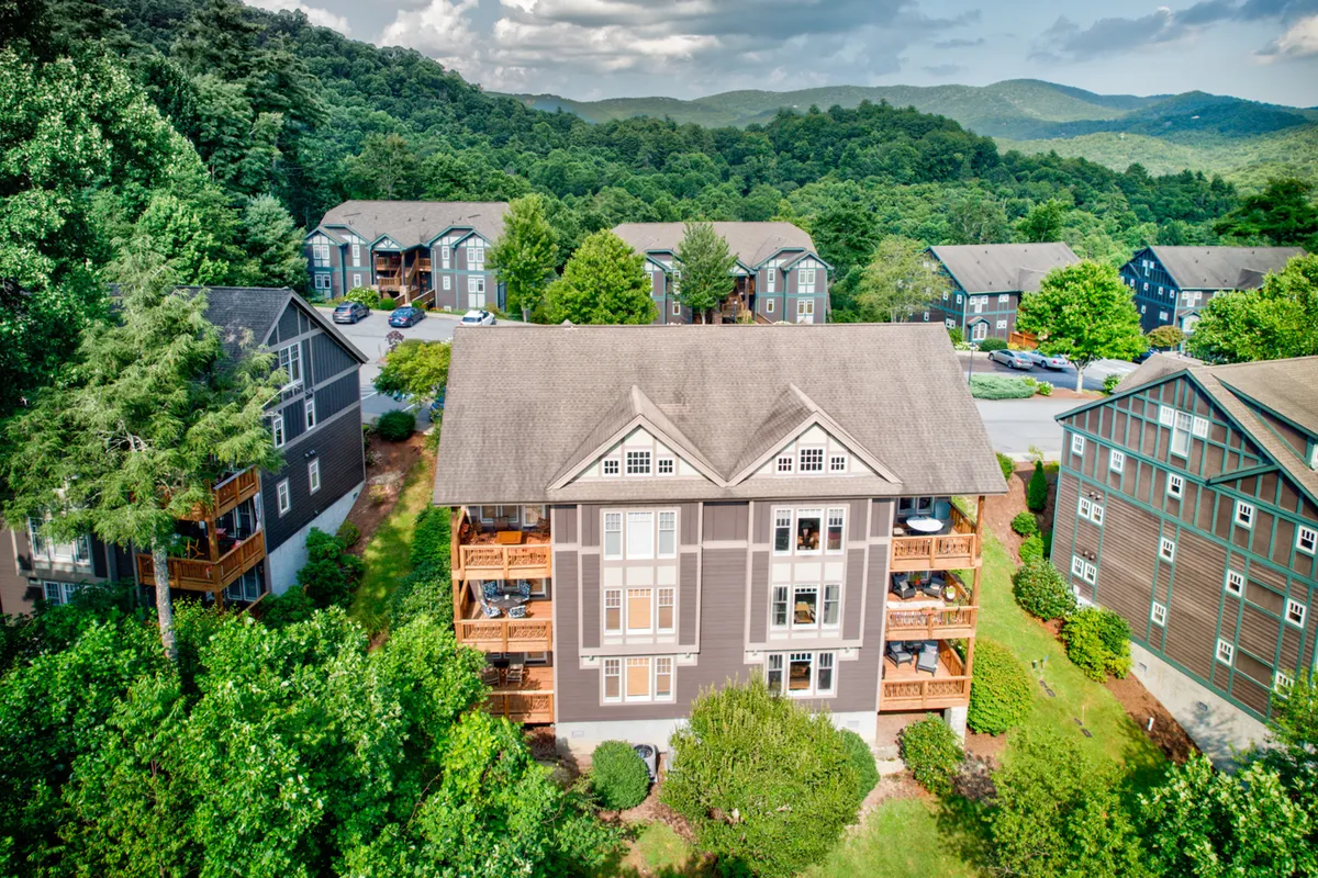 The hero image shows the exterior of a well-maintained condo building nestled amidst lush greenery, with inviting balconies that overlook the majestic Grandfather Mountain. People are seen relaxing on their balconies with coffee and strolling through landscaped paths, all set against a breathtaking mountain backdrop.