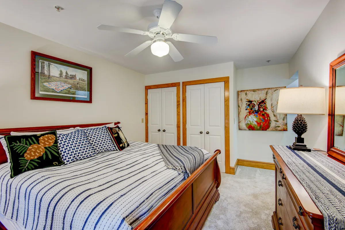 A cozy bedroom with a bed adorned with decorative pillows, a dresser with a lamp, and whimsical owl artwork above the bed. Sunlight streams into the space, enhancing the inviting and restful atmosphere.